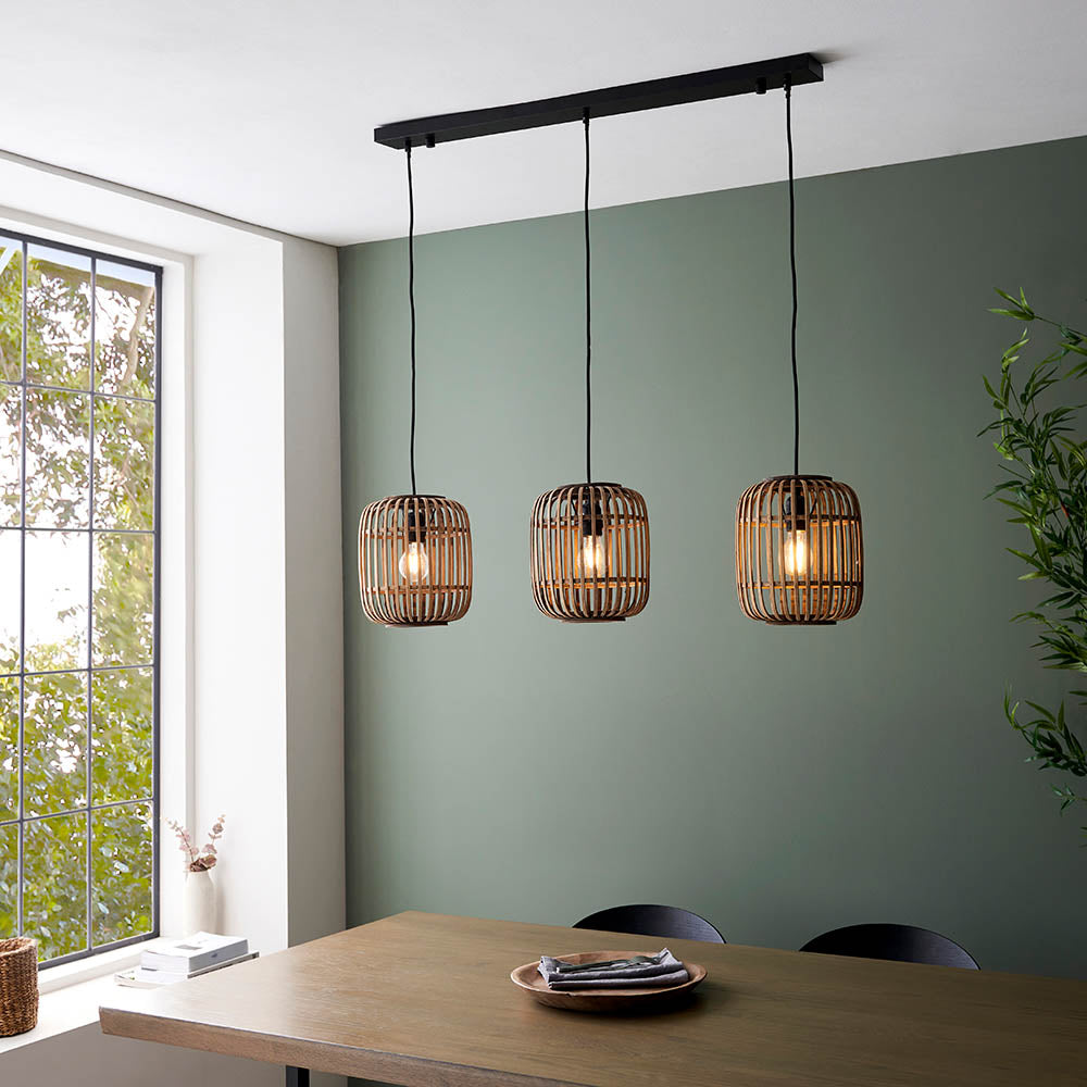 Endon Bracken 3 Light Pendant in black and natural bamboo, linear bar with three slatted cage shades, hung above a wooden dining table by a green wall.