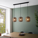 Endon Bracken 3 Light Pendant in black and natural bamboo, linear bar with three slatted cage shades, hung above a wooden dining table by a green wall.