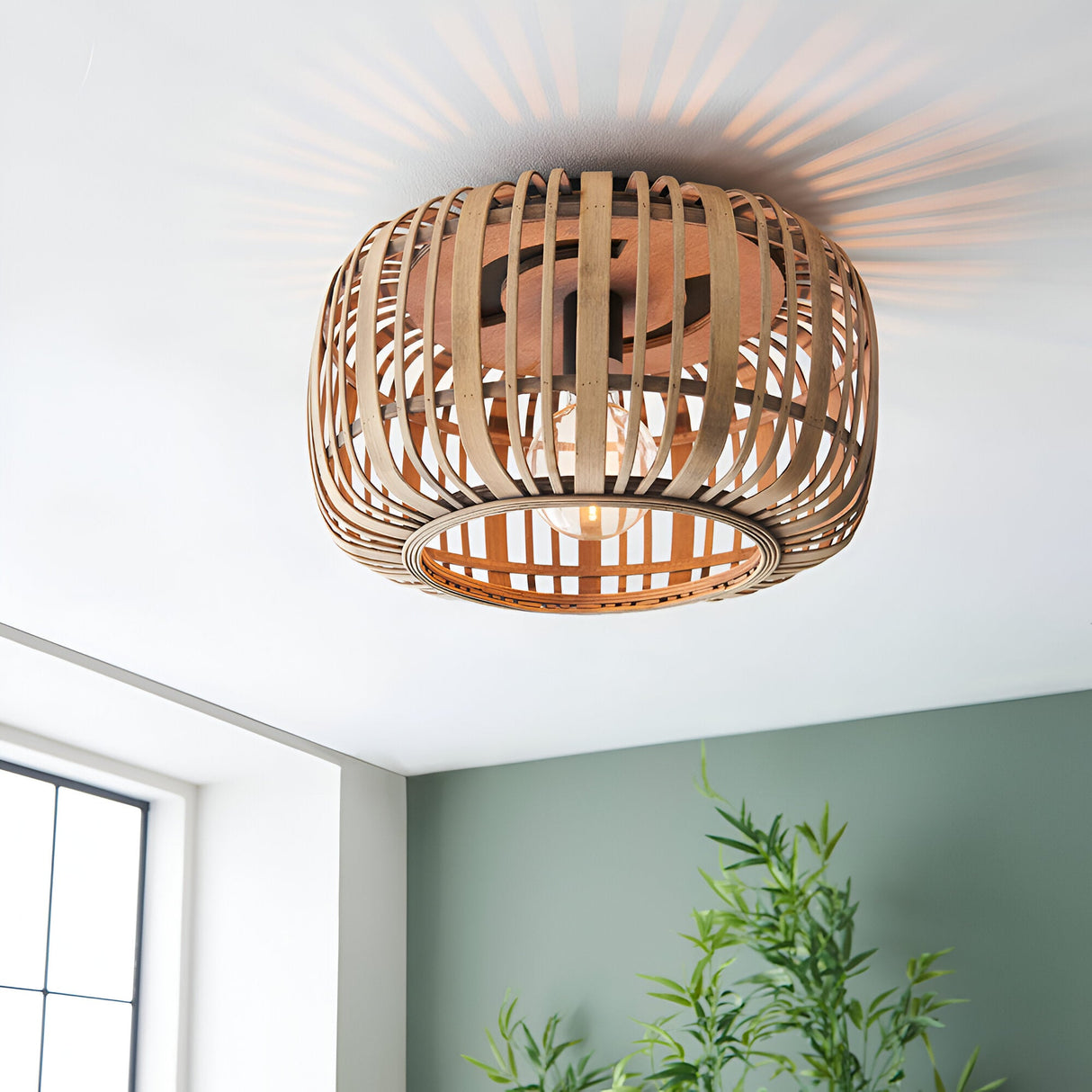 Endon Bracken bamboo flush ceiling light in natural finish, woven drum shade with single E27 lamp, casting radial shadows on the ceiling above a green wall.