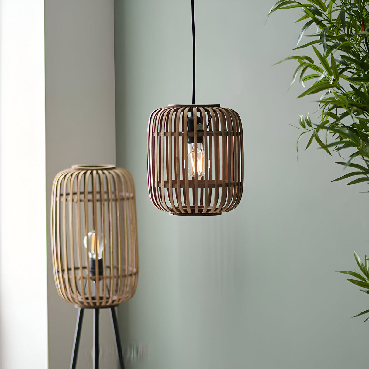 Endon Bracken pendant light with natural bamboo cage shade and matt black flex, shown beside a matching bamboo floor lamp against a sage green wall.