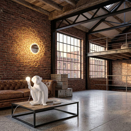 A modern loft with brick walls, large windows, and a mezzanine. The Monkey Sitting Table Lamp - White sits on the coffee table as sunlight streams into the stylish, industrial living space.