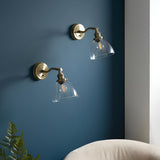 Wentworth Wall Light in antique brass with adjustable knuckle arm and clear glass shade over a filament bulb, shown as a pair on a dark blue wall.