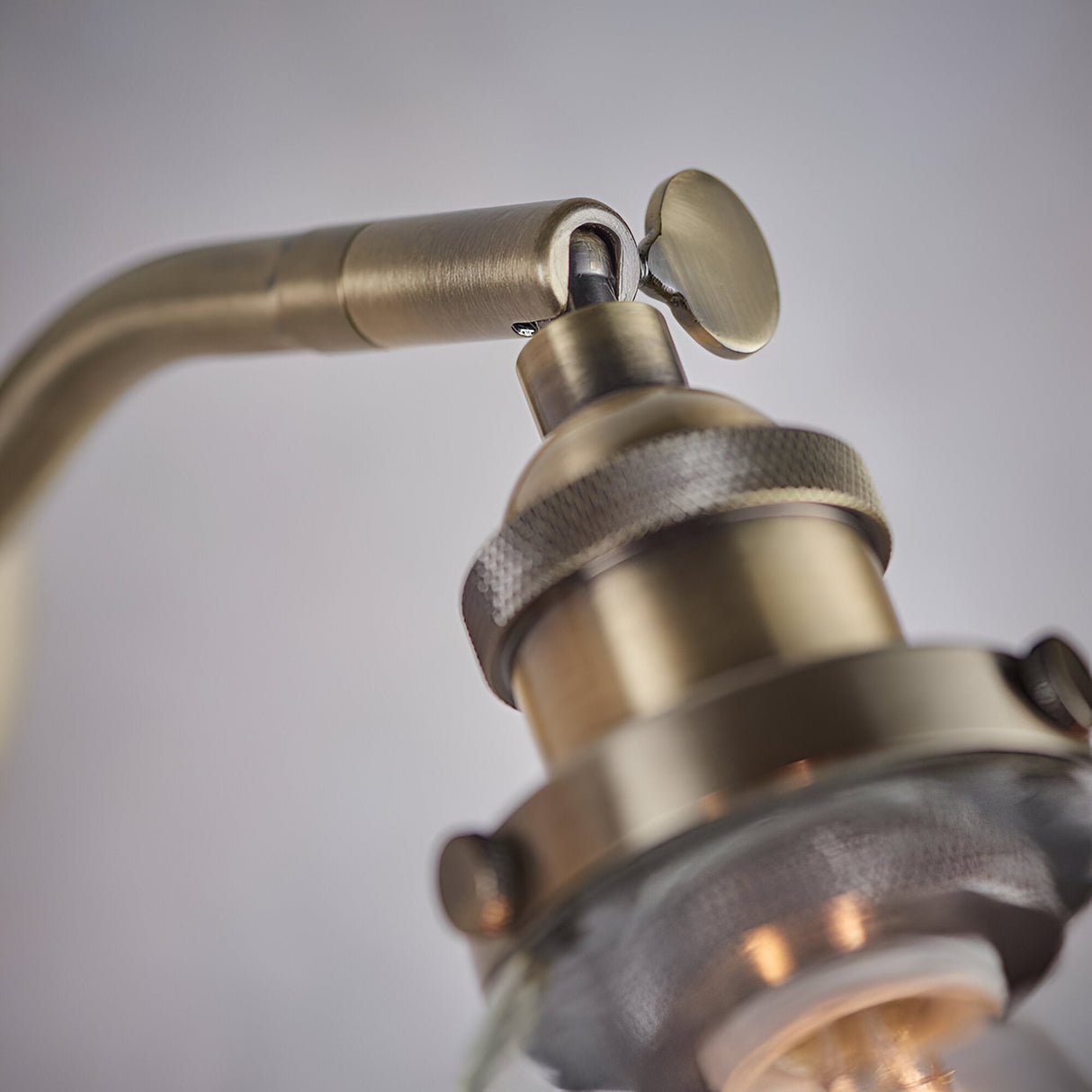 Close-up of the Wentworth Wall Light in antique brass, showing the adjustable knuckle joint, on/off toggle, and knurled lamp holder above a clear glass shade against a plain light background.