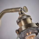 Close-up of the Wentworth Wall Light in antique brass, showing the adjustable knuckle joint, on/off toggle, and knurled lamp holder above a clear glass shade against a plain light background.