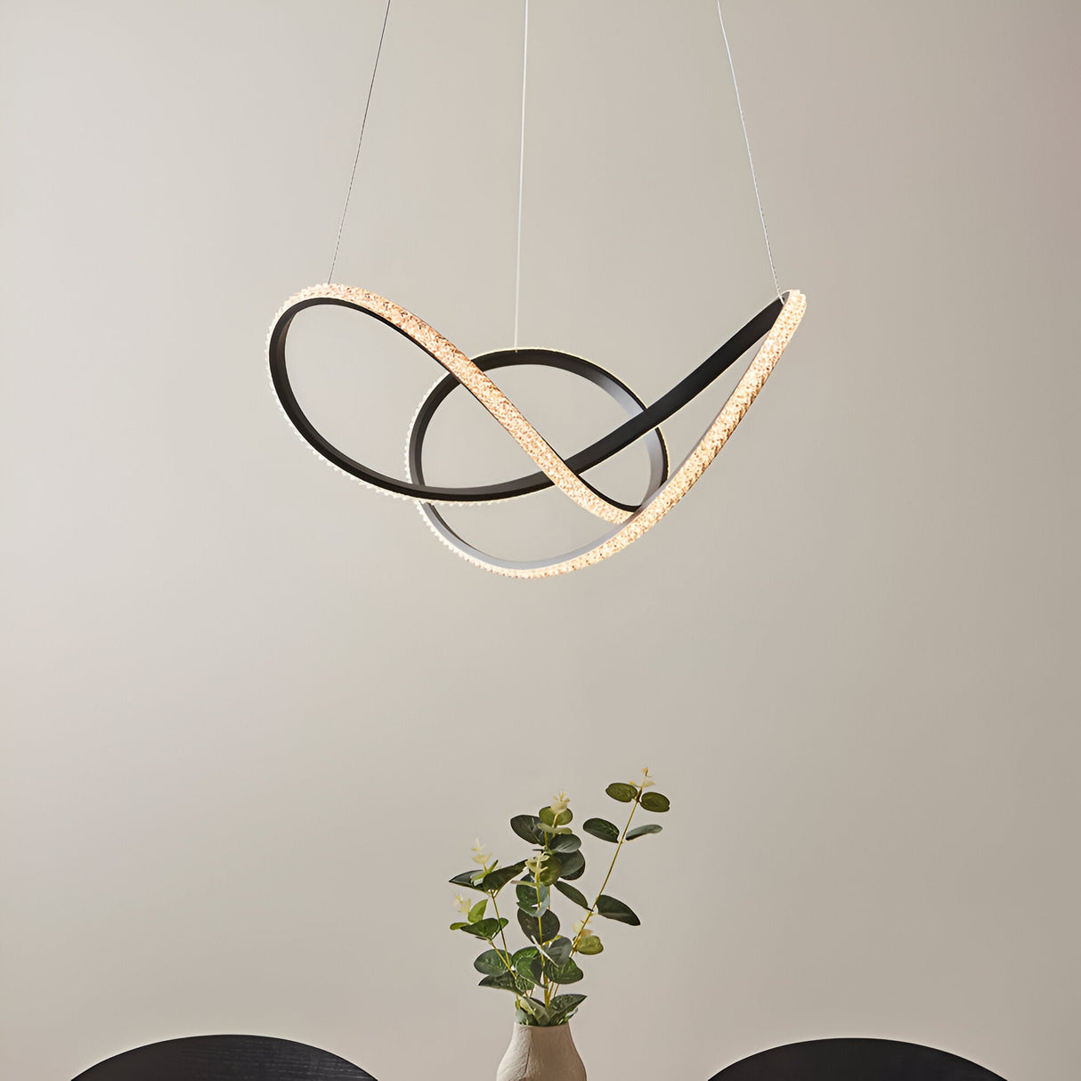 Bramcombe Pendant in black and white featuring interlocking matt black curves with faceted acrylic light strips, suspended above a dining table with a plant.