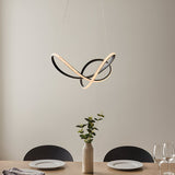 Bramcombe Pendant in matt black with looped, intertwined curves and warm white LED lighting, hung above a dining table in a neutral-toned room.