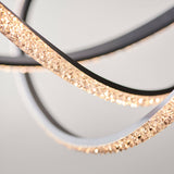 Close-up of the Bramcombe Pendant with curved matt black rings and faceted acrylic crystal detail lit warm white, against a plain light grey background.