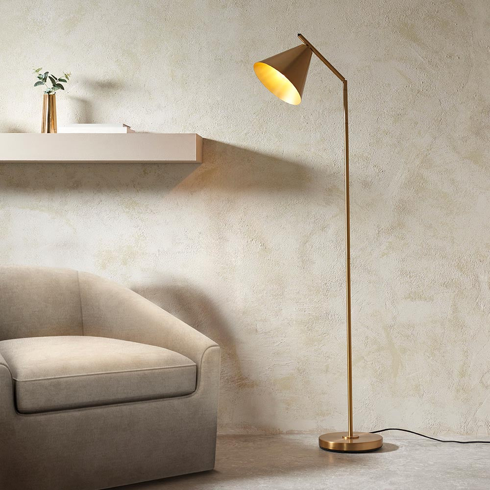 Endon Ashworth floor lamp in antique brass with adjustable arm and conical shade, beside a beige armchair and wall shelf with a vase.