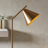 Endon Ashworth floor lamp in brass, with an adjustable arm and conical shade angled downward, set against a neutral plaster wall beside a vase.