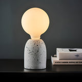 Endon 12W E27 LED filament globe bulb in warm white glowing on a speckled terrazzo lamp base, beside stacked books on a dark shelf.
