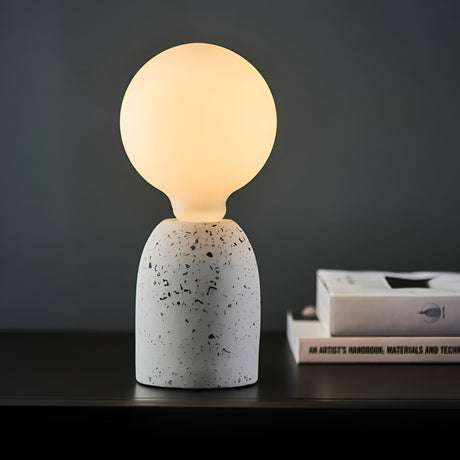 Endon 12W E27 LED filament globe bulb in warm white glowing on a speckled terrazzo lamp base, beside stacked books on a dark shelf.