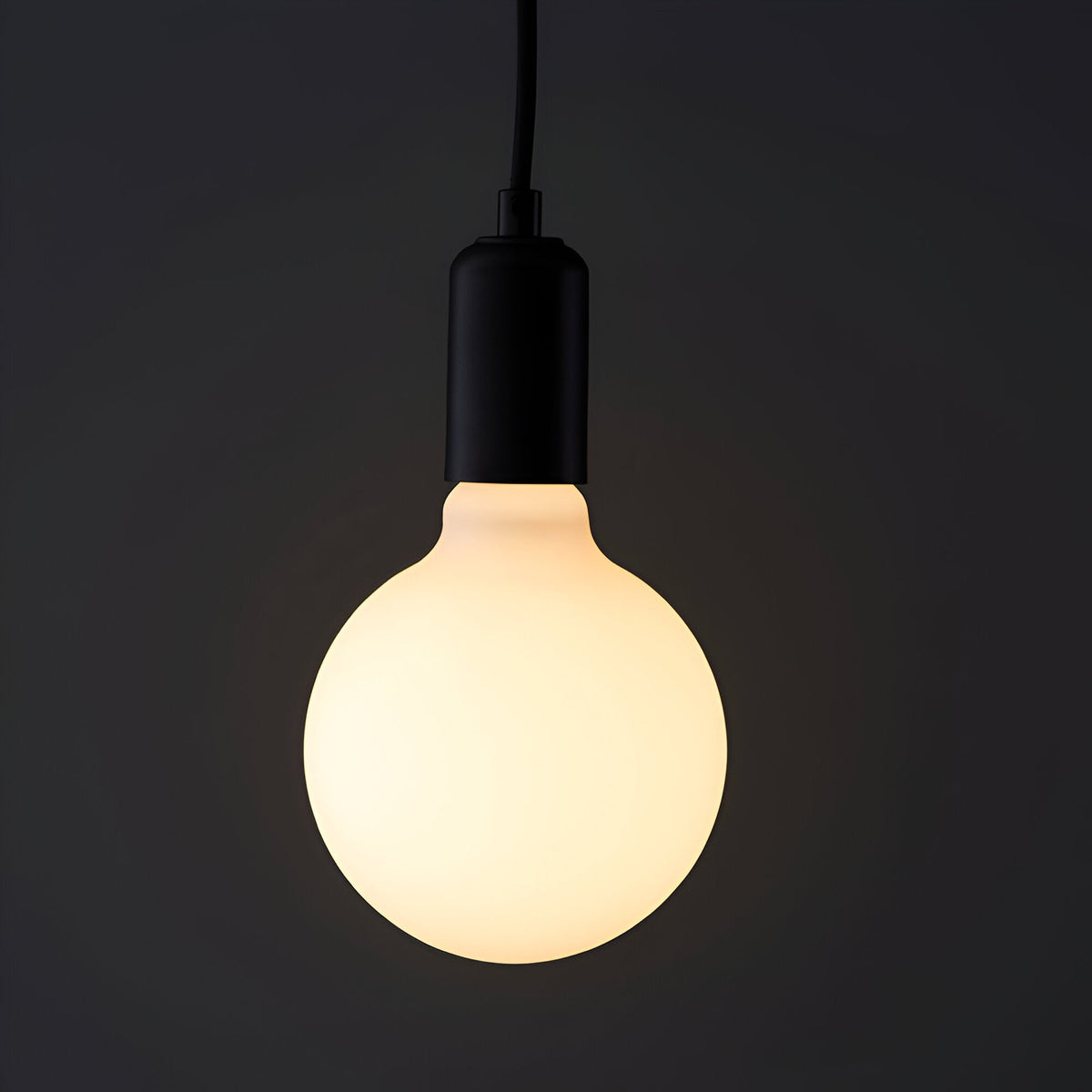 Endon 12W E27 LED filament globe bulb glowing warm white through opal glass in a matte black pendant holder against a dark background.