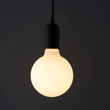 Endon 12W E27 LED filament globe bulb glowing warm white through opal glass in a matte black pendant holder against a dark background.