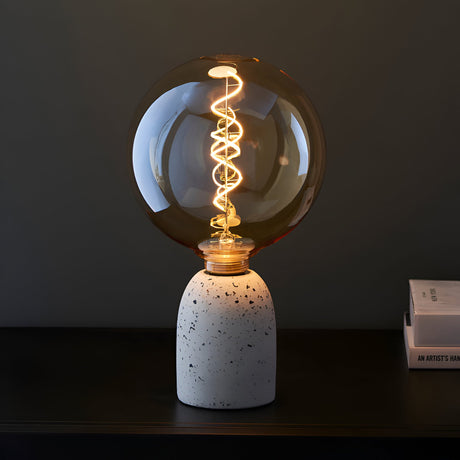Endon 4W E27 LED filament spiral bulb with amber tinted globe glass, illuminated on a speckled terrazzo holder beside books on a dark surface.
