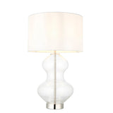 Endon Brockley table lamp with a clear glass hourglass base, polished nickel metalwork and vintage white fabric drum shade on a plain background.