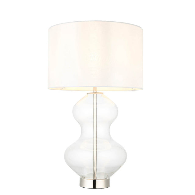 Endon Brockley table lamp with a clear glass hourglass base, polished nickel metalwork and vintage white fabric drum shade on a plain background.