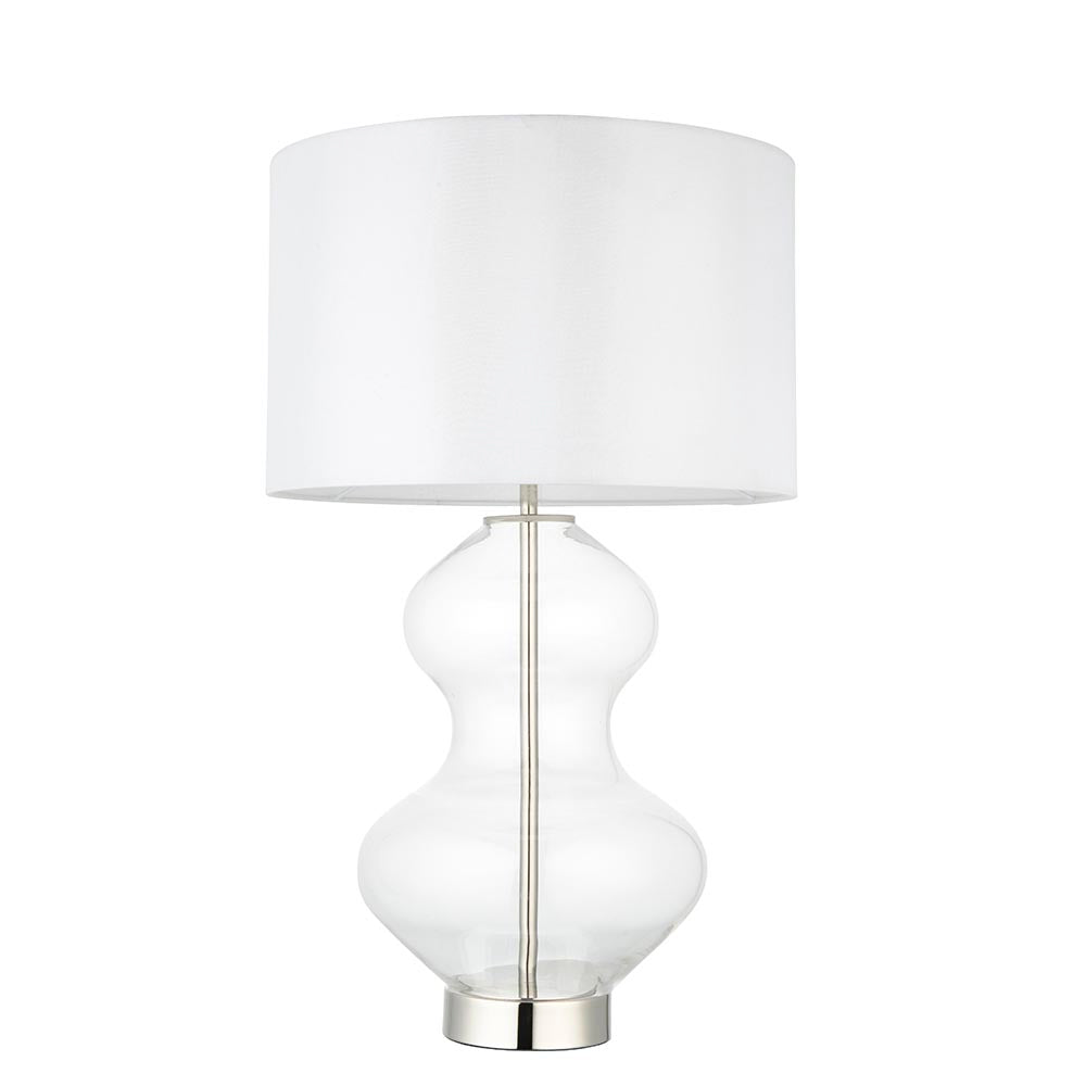 Endon Brockley table lamp with a clear glass hourglass base, polished nickel metalwork and a vintage white fabric drum shade, on a white background.