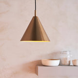 Ashworth Pendant in brass, a cone-shaped single-light fixture with a matching painted inner shade, shown lit above a kitchen shelf with bowls and jars.