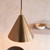 Ashworth Pendant in brass, a single cone-shaped shade with matching painted interior, hung above a shelf styled with bowls in a neutral kitchen setting.