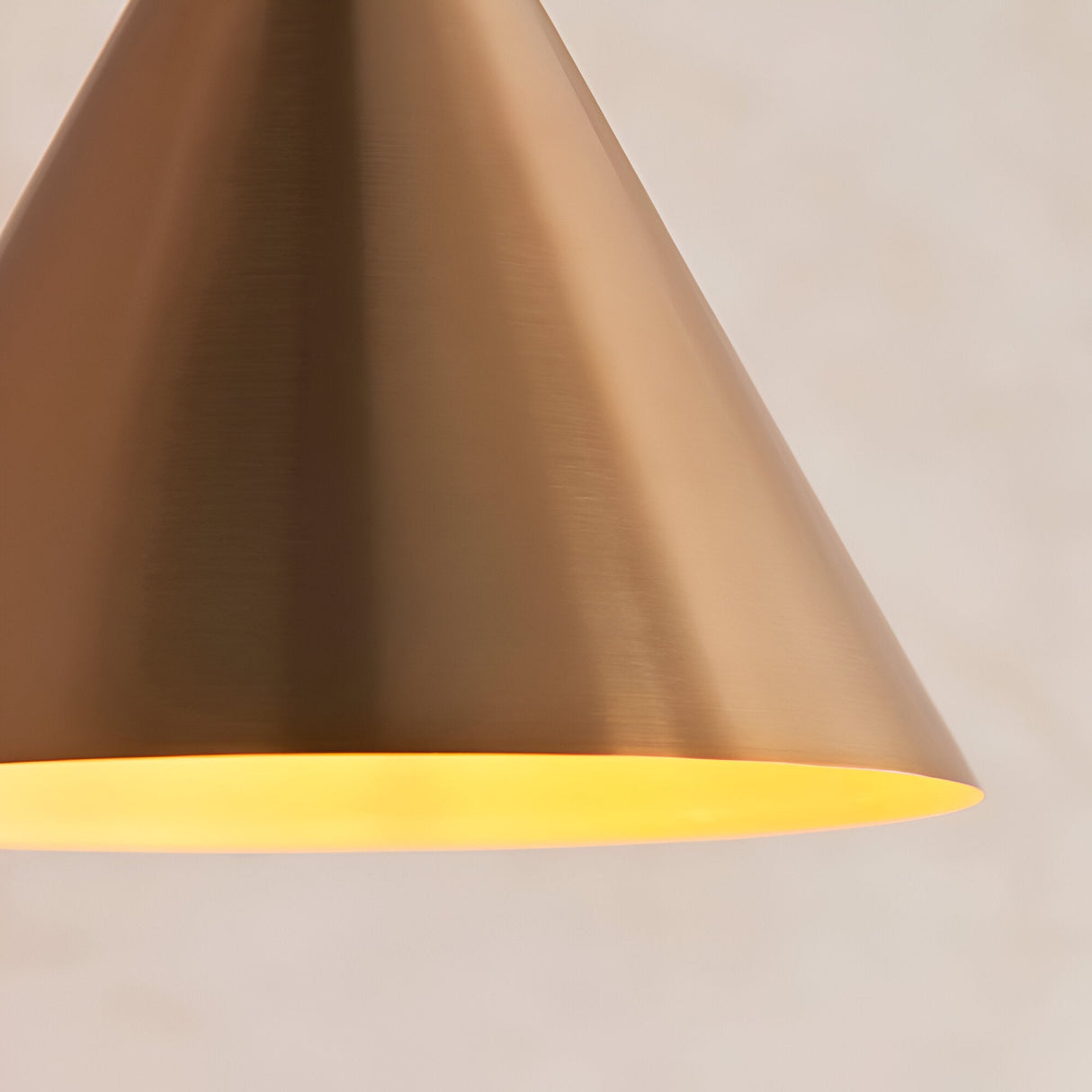 Ashworth Pendant in brass, close-up of the cone-shaped metal shade with warm illuminated inner finish, on a plain light background.