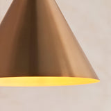 Ashworth Pendant in brass, close-up of the cone-shaped metal shade with warm illuminated inner finish, on a plain light background.