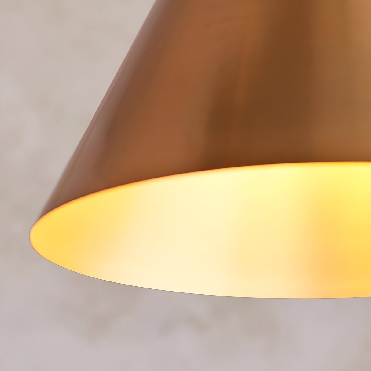 Ashworth Pendant in brass, close-up of the cone-shaped metal shade with matching painted inner and glowing E27 lamp, against a plain light background.