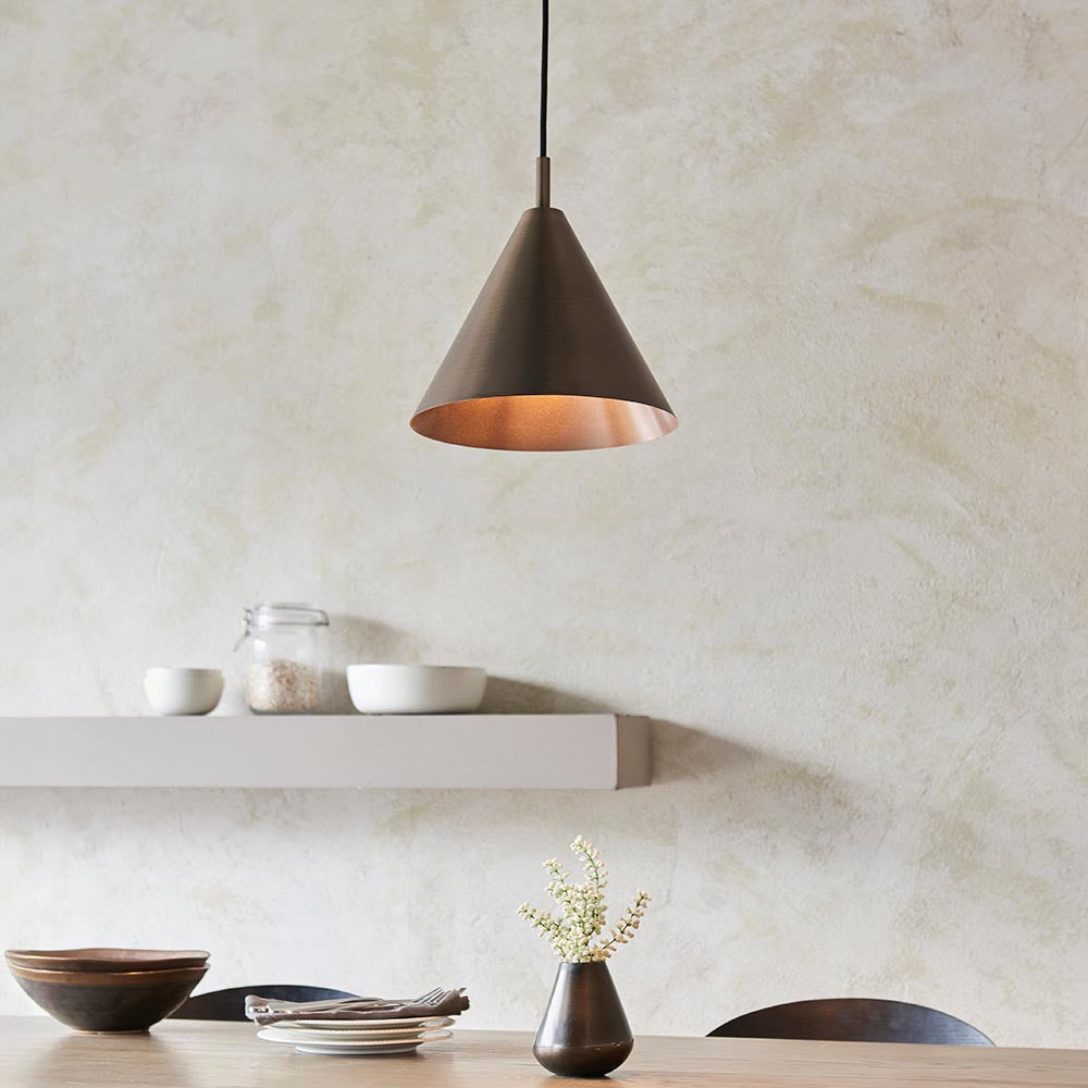 Endon Ashworth bronze pendant light with a conical metal shade and painted copper-toned inner, hung from a black cable above a shelf and dining table.