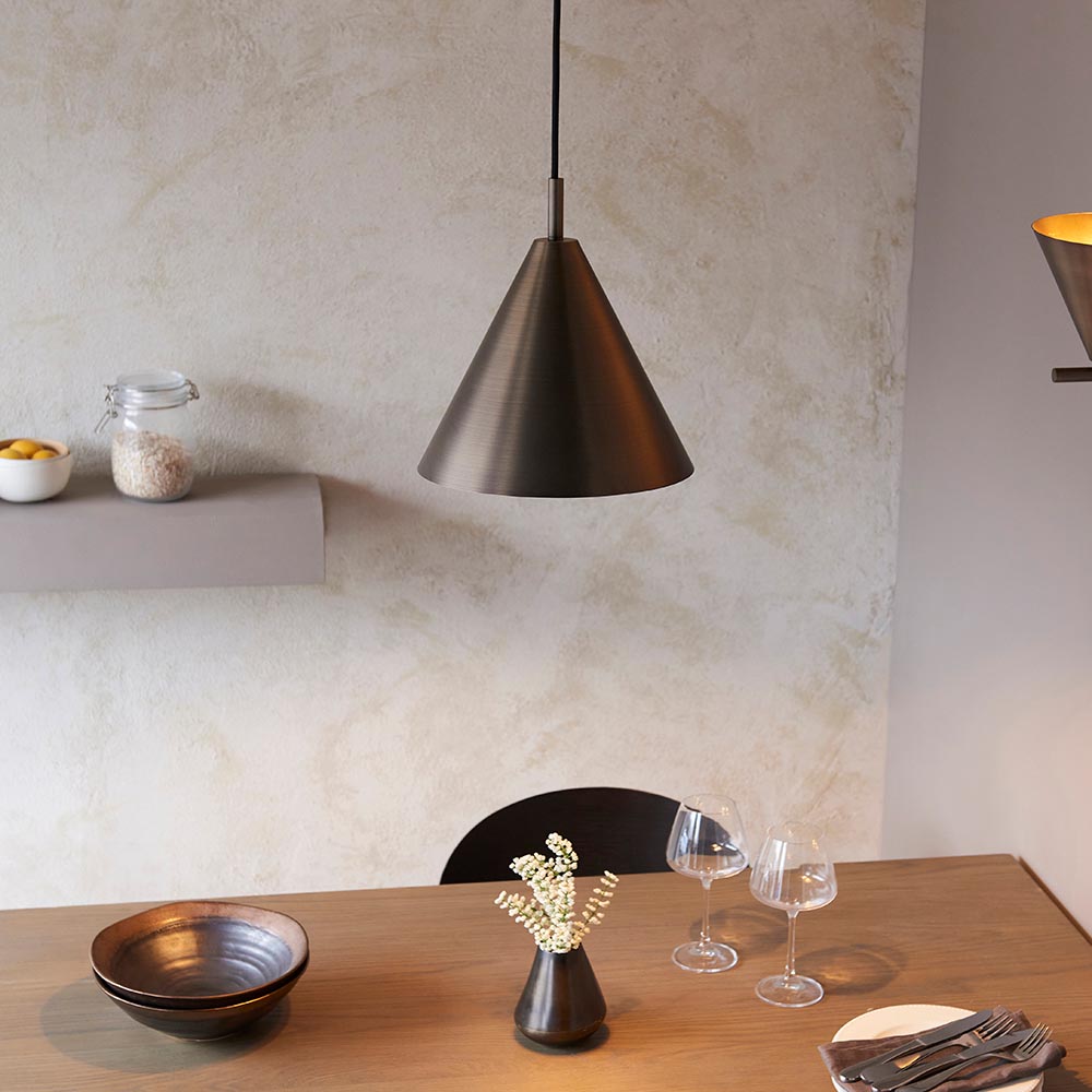 Endon Ashworth bronze pendant light with a conical metal shade and black cable, hanging above a wooden dining table set with bowls, wine glasses, and a vase.
