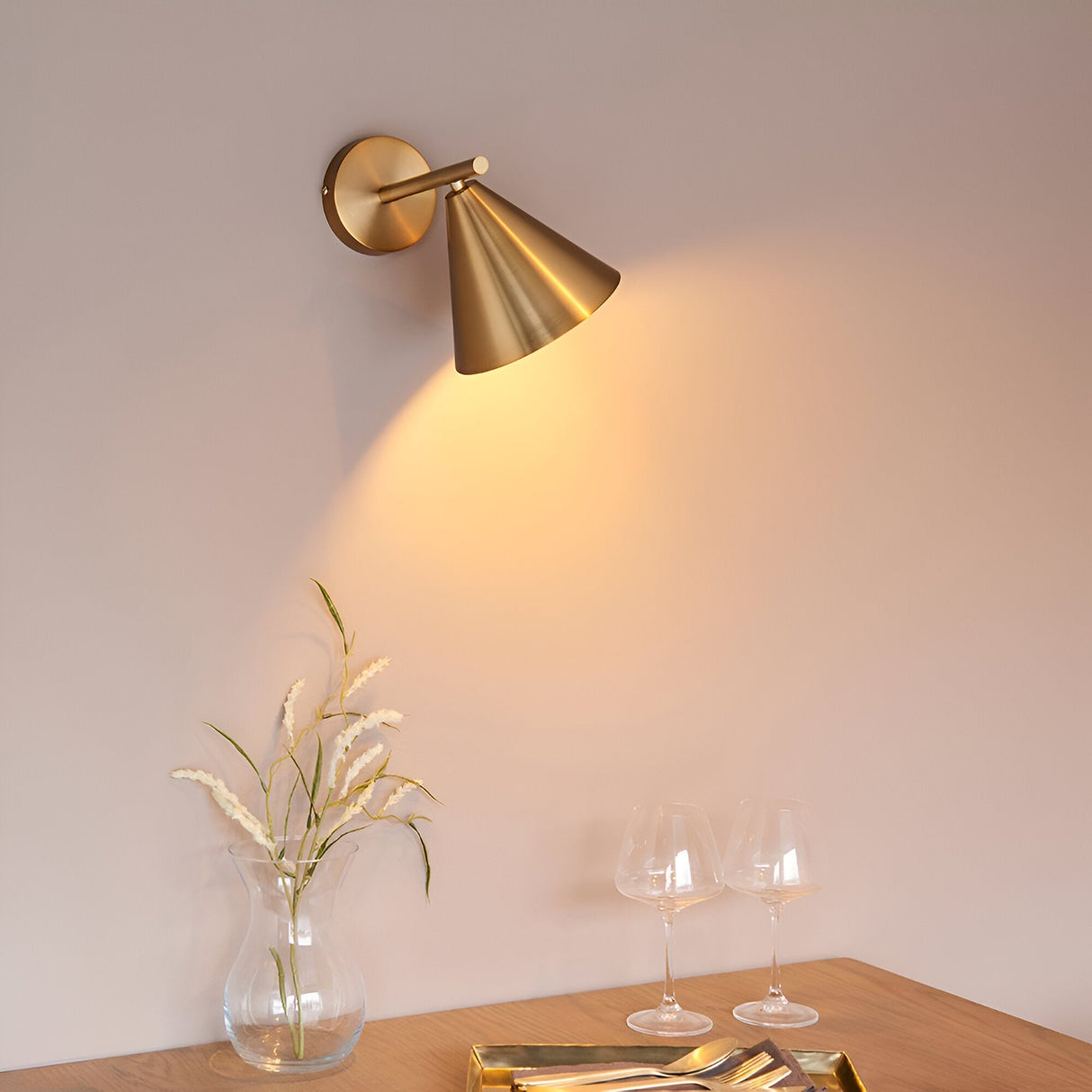 Endon Ashworth brass wall light with adjustable arm and cone shade, illuminating a dining setting with a glass vase and wine glasses below.