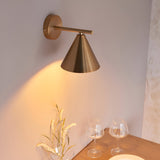 Endon Ashworth wall light in brass with a conical shade and adjustable arm, casting a warm glow above a wooden table set with wine glasses.