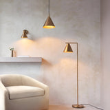 Endon Ashworth brass wall light with conical shade beside a matching pendant and floor lamp, cream armchair and shelf against a textured plaster wall.