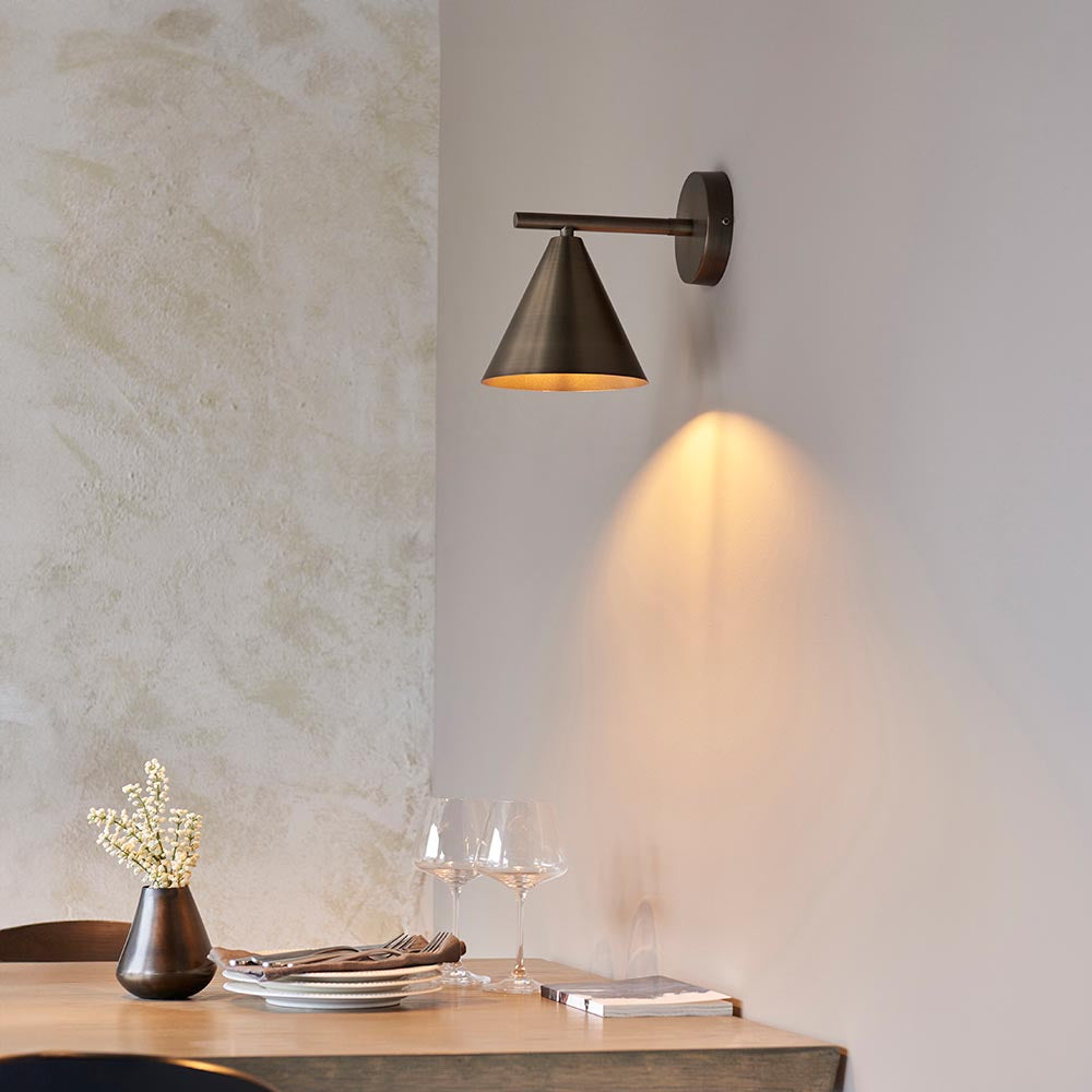 Endon Ashworth bronze wall light with adjustable arm and cone shade, mounted above a wooden dining table with wine glasses and a vase.