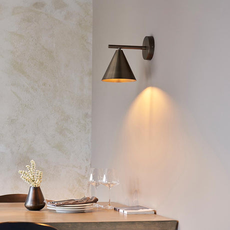 Endon Ashworth bronze wall light with adjustable arm and cone shade, mounted above a wooden dining table with wine glasses and a vase.