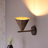 Endon Ashworth bronze wall light with a conical shade on an adjustable arm and round backplate, lit against a pale wall above white flowers.
