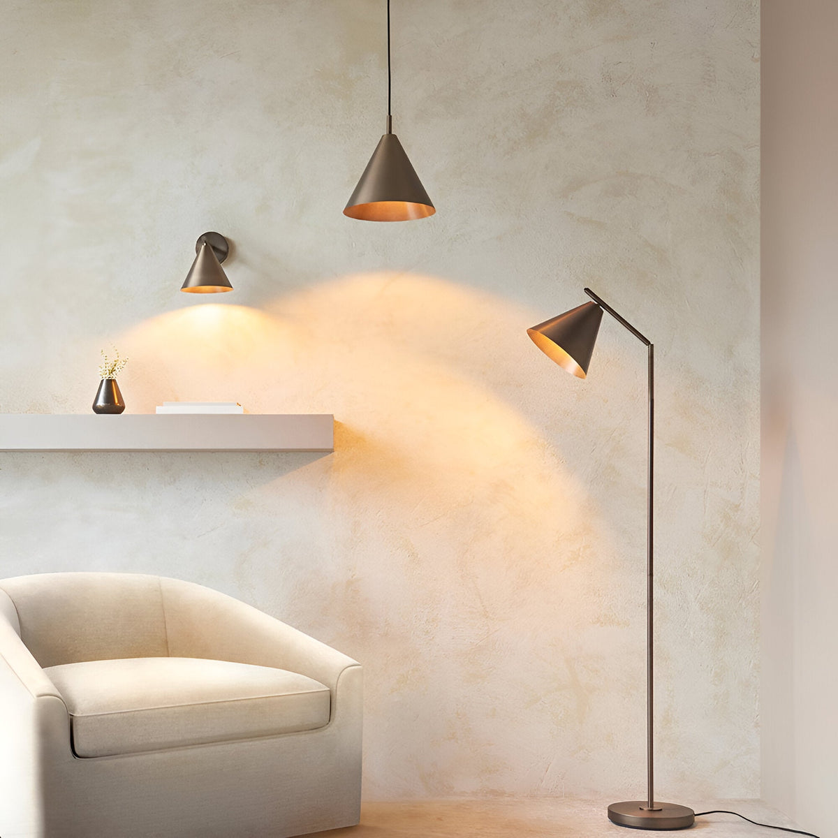 Ashworth Floor Lamp in bronze with adjustable arm and cone shade, shown beside a matching pendant and wall light in a living room setting.