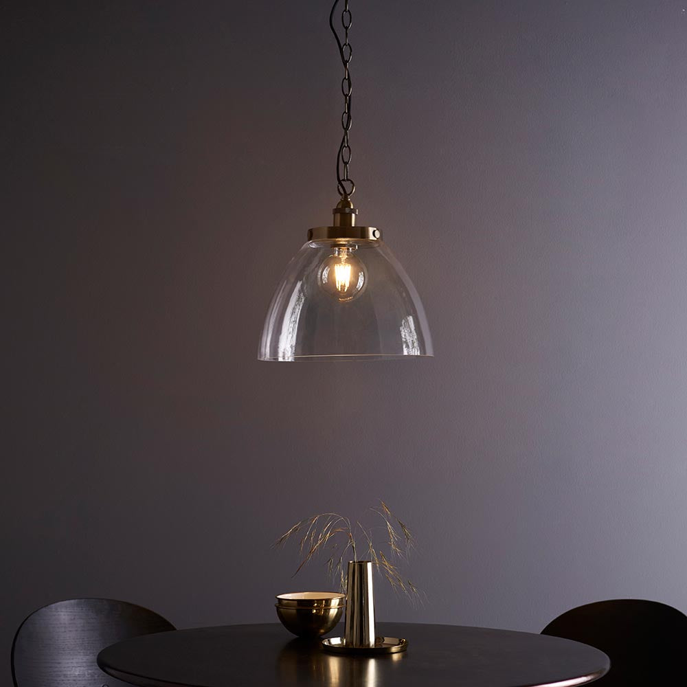Brass Wentworth Pendant with dome clear glass shade, knurled lampholder and filament bulb, hung on a black chain above a dining table.