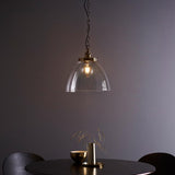 Brass Wentworth Pendant with dome clear glass shade, knurled lampholder and filament bulb, hung on a black chain above a dining table.