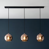 Endon Ashbourne 3 light linear pendant with copper mirrored glass globe shades on a matt black bar, mounted against a two-tone white and navy wall.