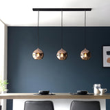 Endon Ashbourne 3 light linear pendant with copper mirrored glass globes on a matt black bar, hung above a dining table against a dark blue wall.