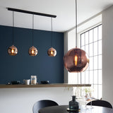 Endon Ashbourne 3 light linear pendant with copper mirrored glass globes on matt black bar, shown beside a larger copper globe pendant in a dining space.