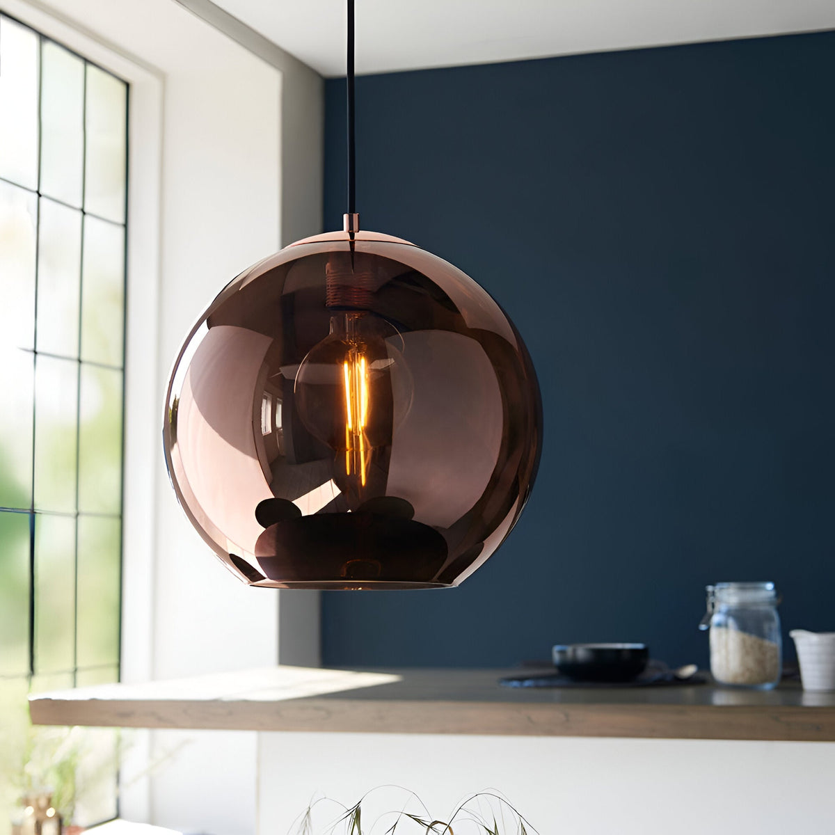 Endon Ashbourne pendant light with a single copper mirrored glass globe shade and black cable, hanging above a kitchen counter against a dark blue wall.