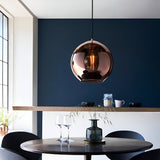 Endon Ashbourne pendant with a single copper mirrored glass globe shade and black cable, hung above a round dining table against a deep blue wall.