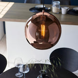 Endon Ashbourne pendant with a copper mirrored glass globe shade and black cable, lit above a dining table with wine glasses and grasses.