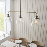 Endon Wentworth 3 light linear stem pendant in antique brass with clear glass dome shades and exposed filament bulbs, hung above a dining table.