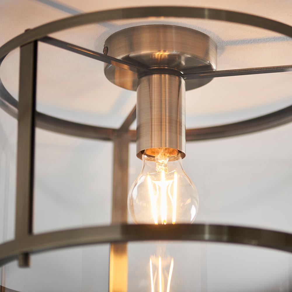 Close-up of Endon Ellery flush ceiling light in brass, showing the E27 lamp holder, exposed filament bulb and circular glass shade frame.
