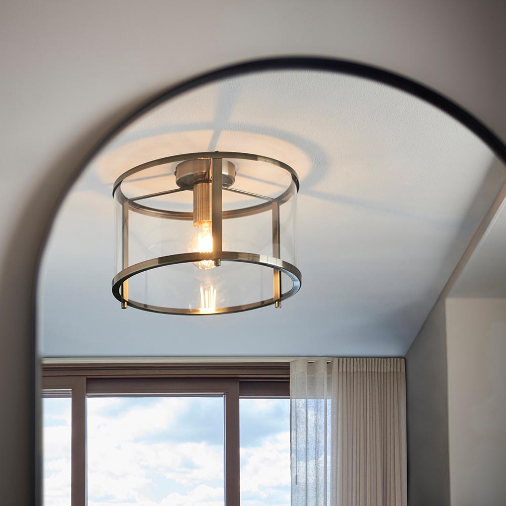 Endon Ellery flush ceiling light in brass with a cylindrical clear glass shade and single E27 lamp, mounted on a ceiling above an arched doorway.