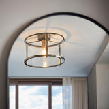 Endon Ellery flush ceiling light in brass with a cylindrical clear glass shade and single E27 lamp, mounted on a ceiling above an arched doorway.