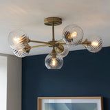 Endon Georgiana 6 light semi-flush ceiling light in brass with ribbed glass globe shades on angled arms, installed against a navy blue wall.