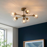Endon Georgiana 6 light semi-flush ceiling light in brass with ribbed glass globe shades, mounted on a ceiling above a dark blue wall.
