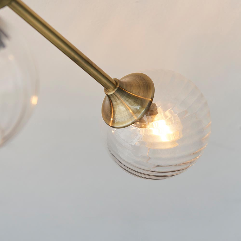 Close-up of one arm of the Endon Georgiana 6 Light Semi-Flush Ceiling Light in brass, showing a ribbed clear glass globe shade and lit E14 lamp.